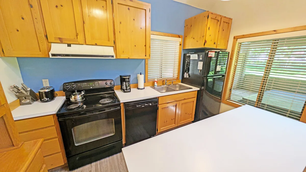 The kitchen area is equipped with black appliances, wooden cabinetry, and a bright window, providing a practical and inviting space for meal preparation and family gatherings.