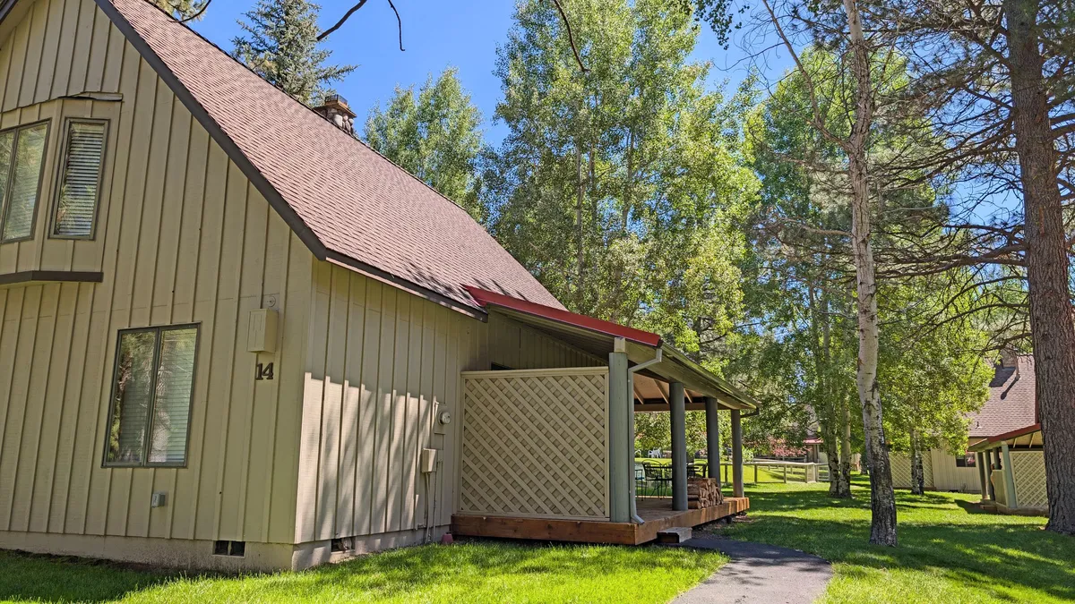 This exterior image highlights the cabin's structure nestled among tall trees, with a welcoming porch area that invites relaxation. The surrounding natural environment suggests a tranquil resort setting and hints at outdoor recreational opportunities.