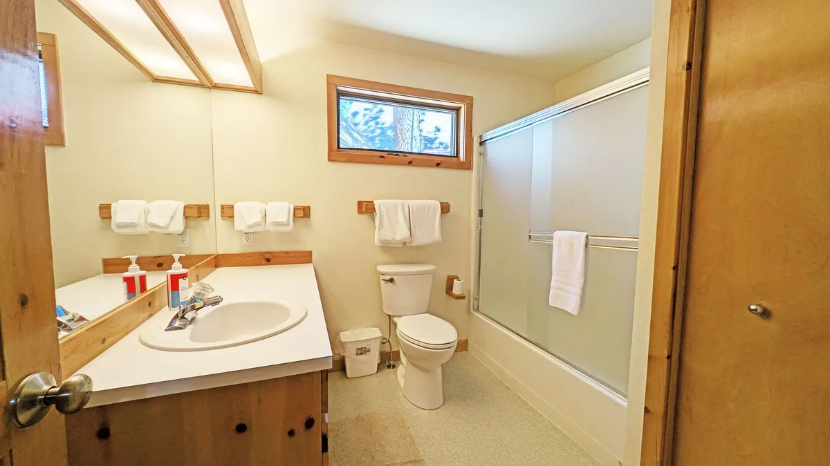 A light-filled bathroom with a modern vanity and sink, a glass shower enclosure, and a window that lets in natural light. The space is clean, calm, and features plush towels for guest use.