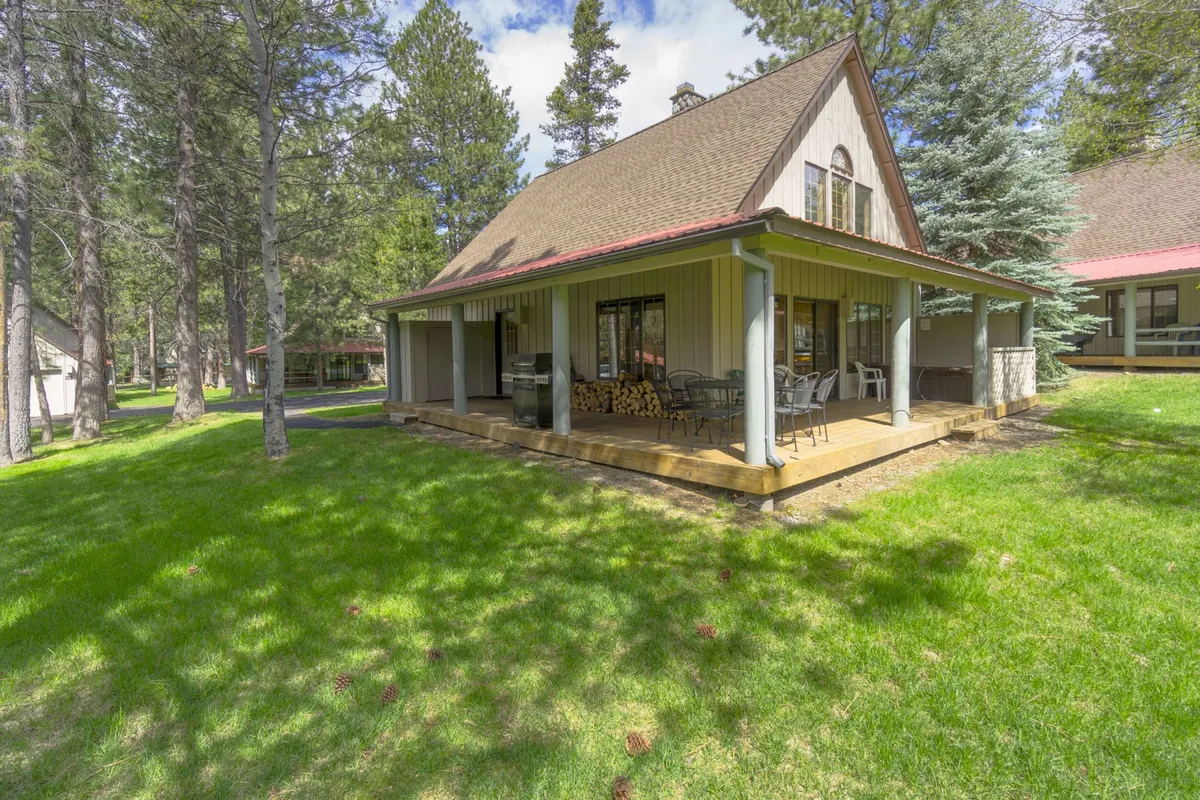 This exterior image captures the front porch, a wood stack, and expansive windows, all set within a peaceful, tree-filled environment. The space feels inviting and close to nature—ideal for returning from a day at the SHARC or Sunriver’s community activities.