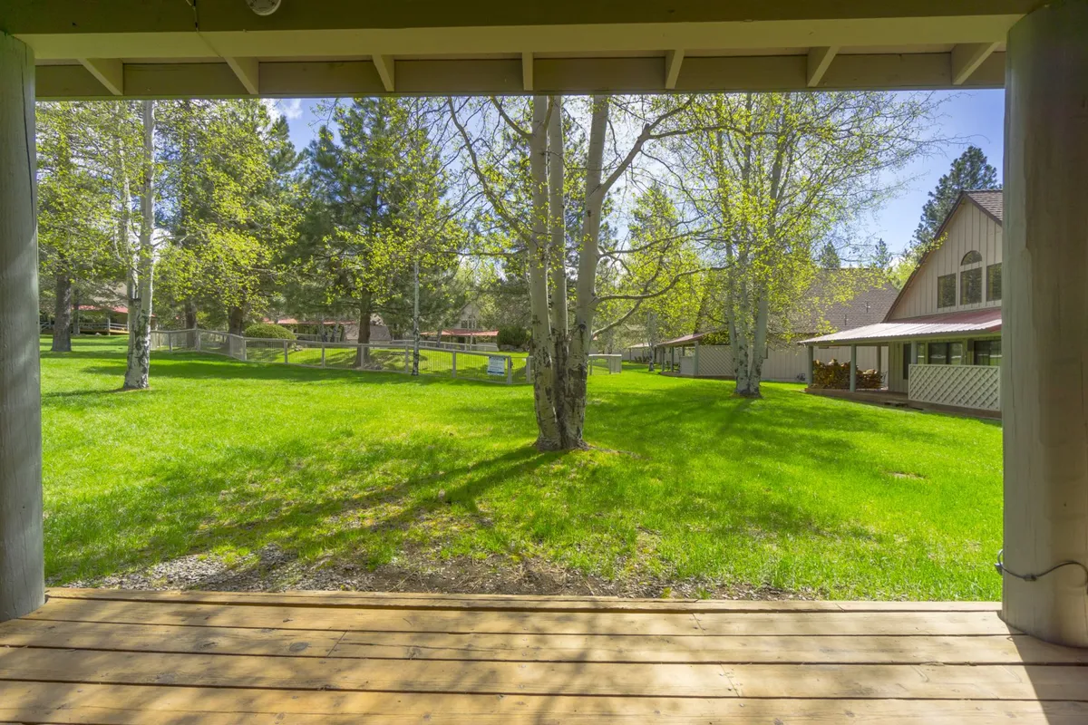 A view of a lush green lawn framed by soaring trees and a wooden deck, providing an expansive outdoor play area for families and an inviting spot for picnics or casual gatherings.