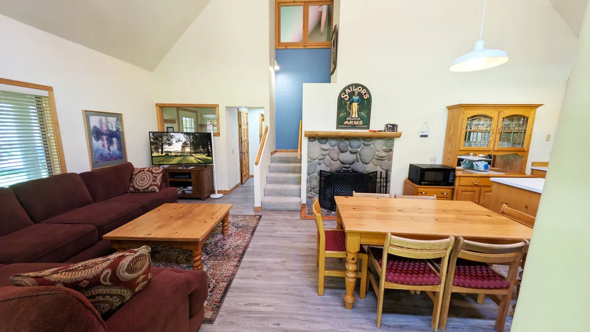This image showcases the main living area with a comfortable sofa, dining table, fireplace, television, and a staircase. The open layout hints at a communal space designed for gatherings, relaxation, and shared meals—central to an affordable, adventure-focused getaway.