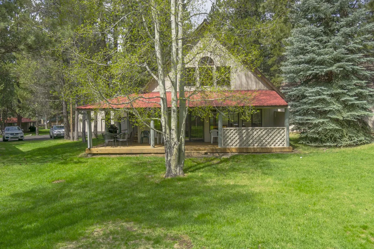This image displays the exterior of the condo with its distinctive red roof, surrounded by mature trees and a well-kept lawn. The welcoming porch invites families to relax and enjoy the natural setting, providing a sense of the tranquil, community-oriented environment central to Sunriver.