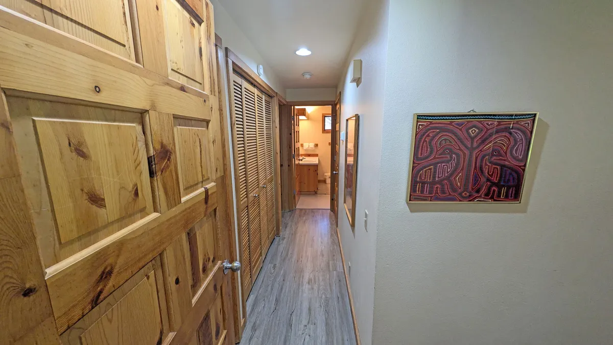 This image shows an inviting entrance hallway with warm wooden doors, artistic wall décor, and soft lighting fixtures. The view suggests movement towards other parts of the home, subtly hinting at transitions between indoor comfort and outdoor adventure.
