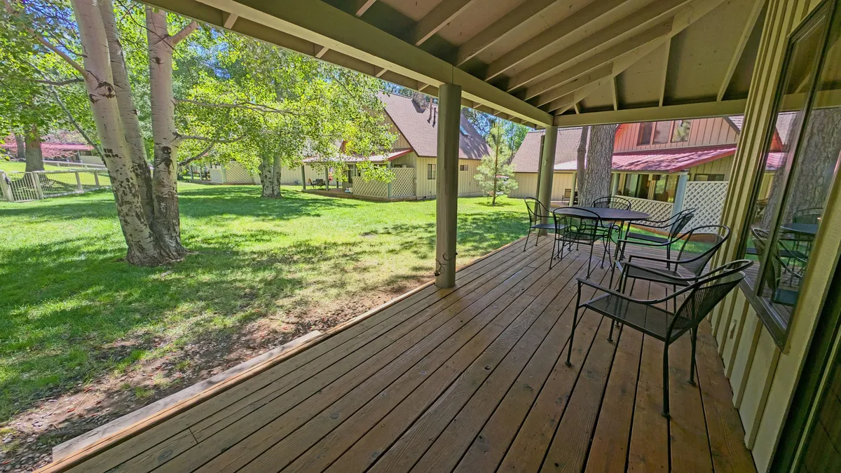 A tranquil wooden deck with metal chairs overlooks a lush green lawn and is surrounded by tall trees. The space is designed for outdoor dining, relaxation, and taking in the natural setting, illustrating the potential for morning coffee or stargazing as described in the section.