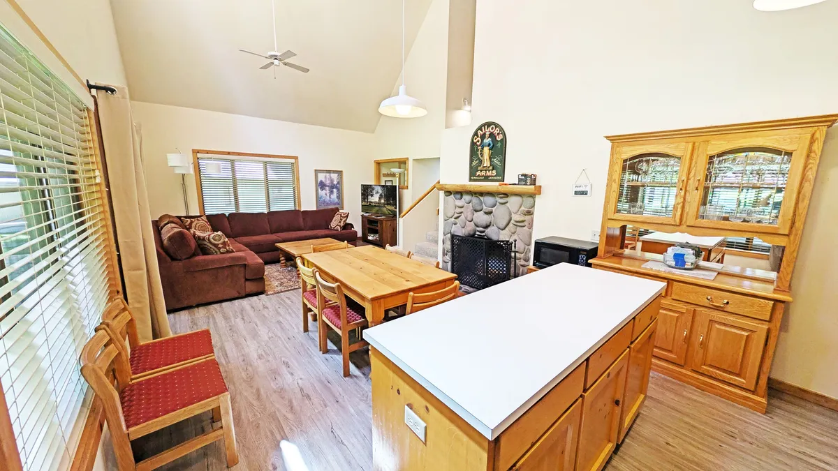 This image highlights the seamless connection between the sofa area, dining table, kitchen island, and a fireplace. The room glows with an inviting atmosphere, making it ideal for both everyday relaxation and special celebrations.