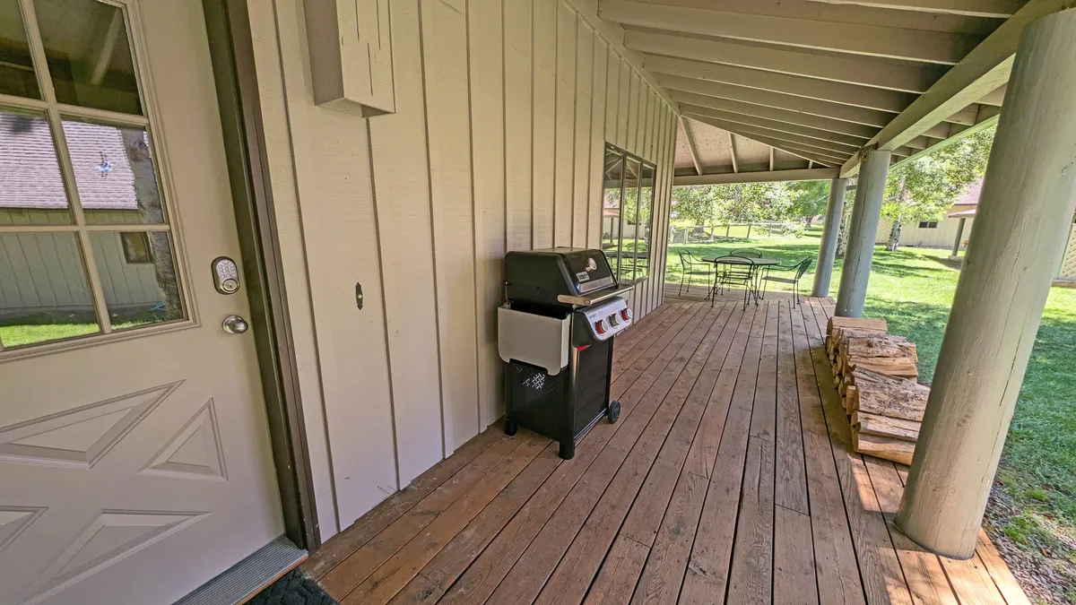 A casual outdoor setup with a grill, patio furniture, and a wood pile situated on a wooden patio. The scene invites guests to cook, dine, and spend time outside, highlighting the grill and the inviting nature of the deck area.